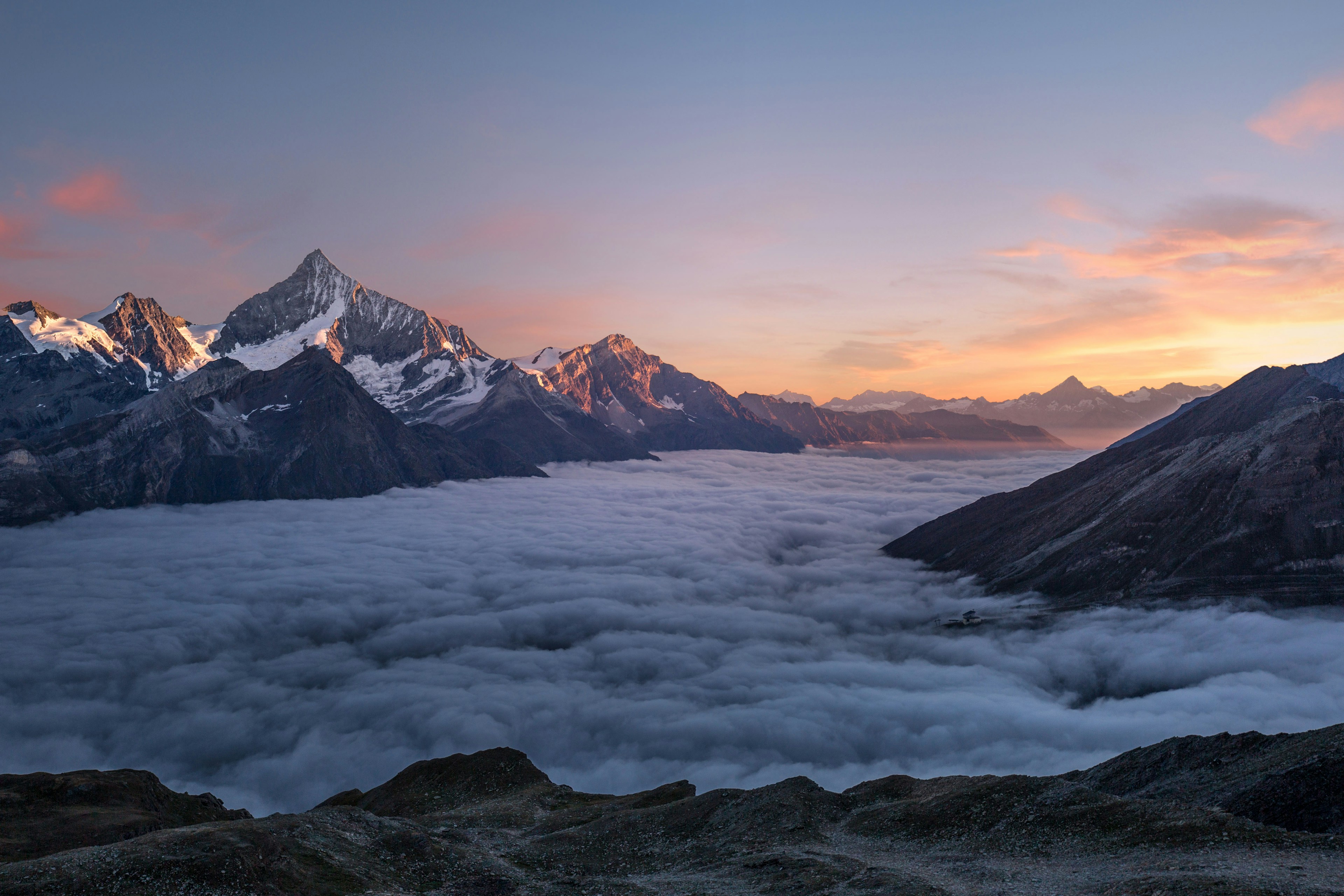 Snow covered alpine peaks above a sea of clouds at sunrise